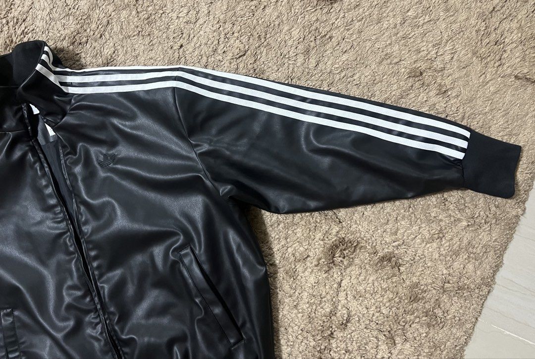 Adidas Leather Jacket with Stripes (Category: Coats, Jackets and Outerwear) located in Manila. Submitted by cluttercrushers (Listing ID 1422009596, Image 2). Description: - Adidas jacket features a sleek black leather design with the iconic three stripes on the sleeves. - It has a full zip closure, a stand-up collar, and the Adidas logo on the chest. - The jacket includes two front pockets and ribbed cuffs and hem for a comfortable fit. The tags 