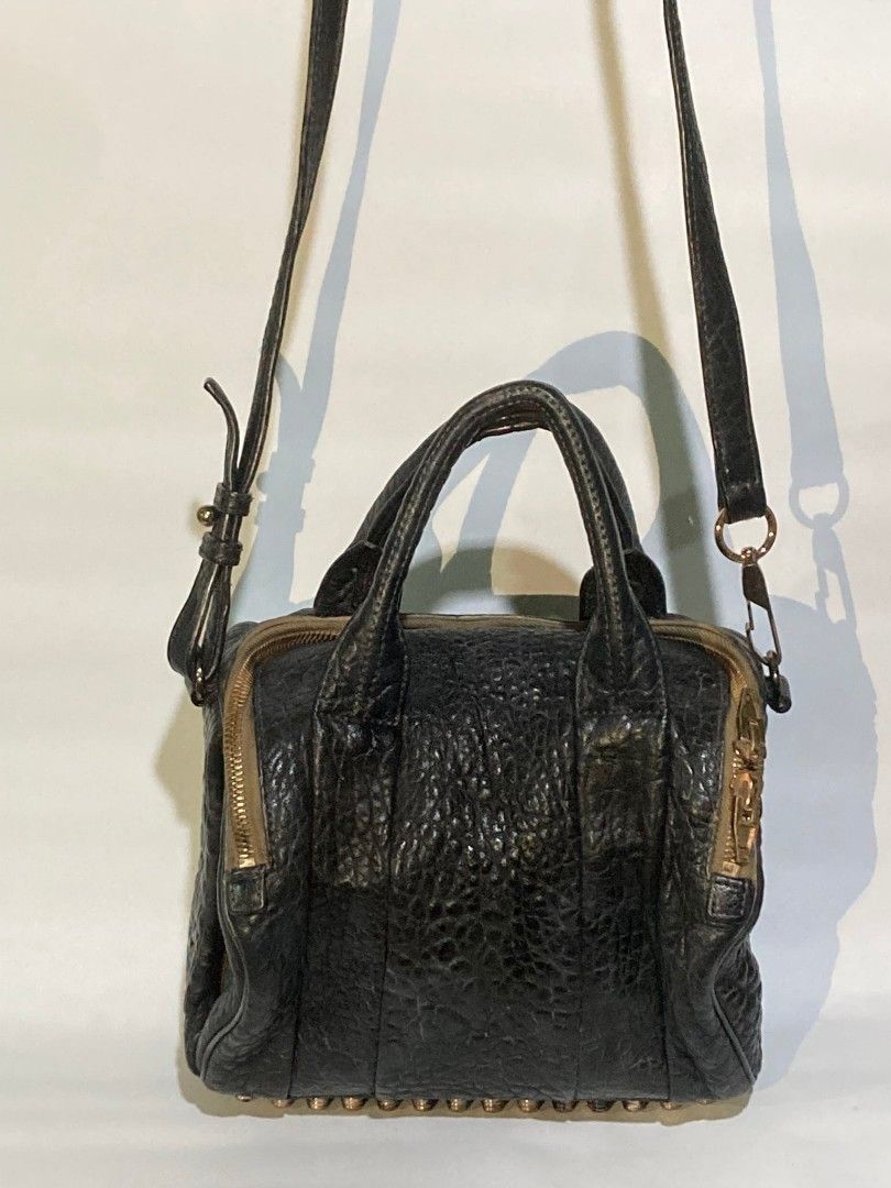 Alexander Wang Rocco Duffel Bag (Category: Luxury Bags & Wallets) located in Taguig. Submitted by blessedlupie (Listing ID 1422026096, Image 1). Description: Black Alexander Wang Rocco Duffel bag with gold-tone hardware. Features a top handle and a detachable shoulder strap. The bag has a textured leather exterior with a zip closure. The base of the bag has metal studs..
