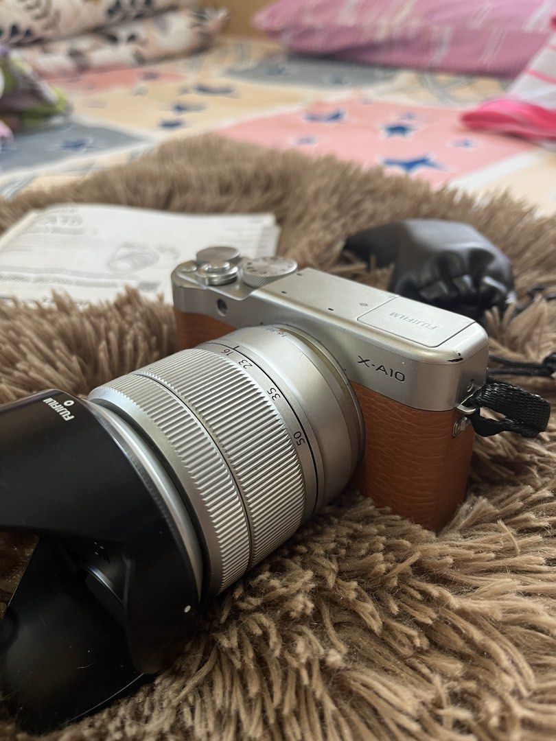 Fujifilm X-A10 Digital Camera (Category: Cameras) located in San Ildefonso. Submitted by happybev23 (Listing ID 1421963579, Image 2). Description: - Fujifilm X-A10 digital camera - Includes lens and lens cap - Comes with owner's manual - Silver body with brown leather grip - Lens has a black hood - Comes with charging cord only Note: leather strap is peeling, scratches on body.