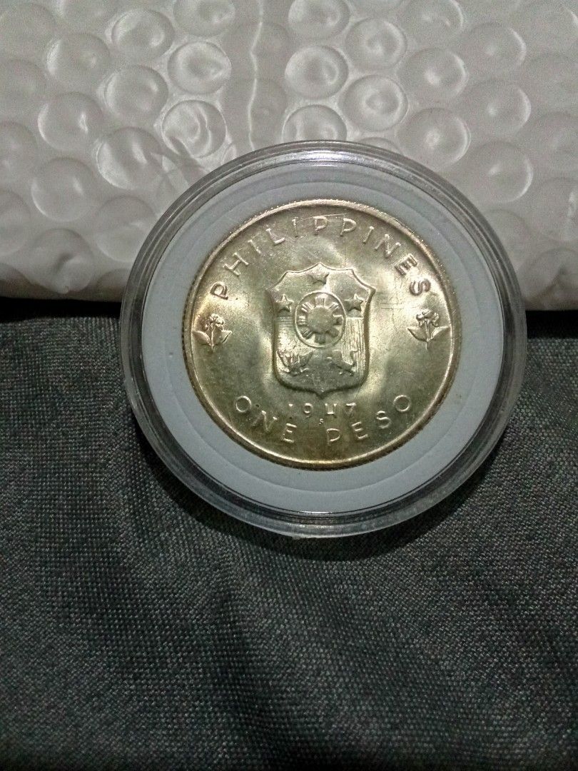 1947 Philippines One Peso Coin (Category: Currency) located in Quezon City. Submitted by mogan27 (Listing ID 1422174338, Image 2). Description: - 1947 One Peso coin from the Philippines. - Features Douglas MacArthur on one side. - Displays the Philippine coat of arms on the other. - Preserved in a protective plastic holder..