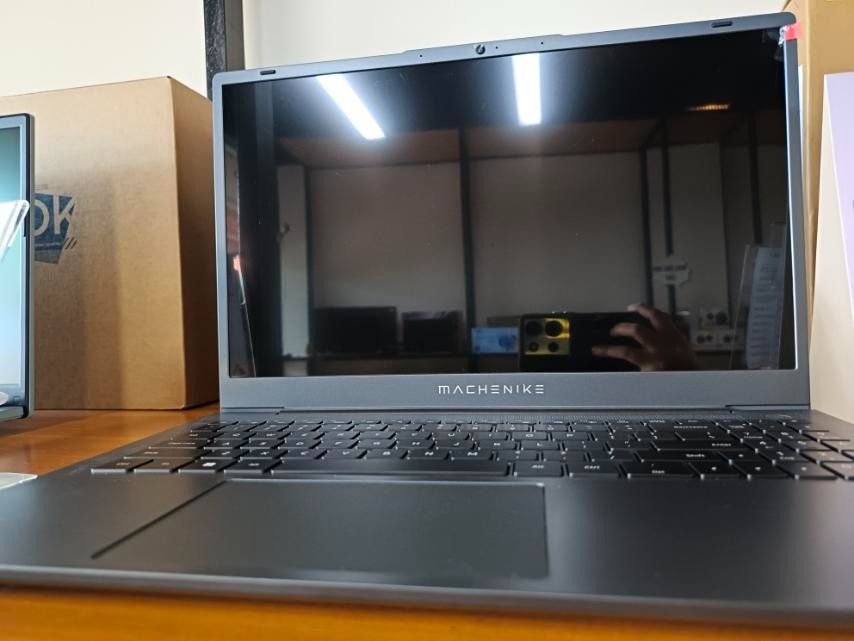 Machenike MC15A (Category: Laptops & Notebooks) located in Caloocan City. Submitted by ahuboutletstore (Listing ID 1422136560, Image 1). Description: Machenike laptop with a sleek, dark design. Features a full keyboard and a large trackpad. The screen is glossy. The laptop is on a wooden surface. The brand name "Machenike" is visible on the laptop's bezel..