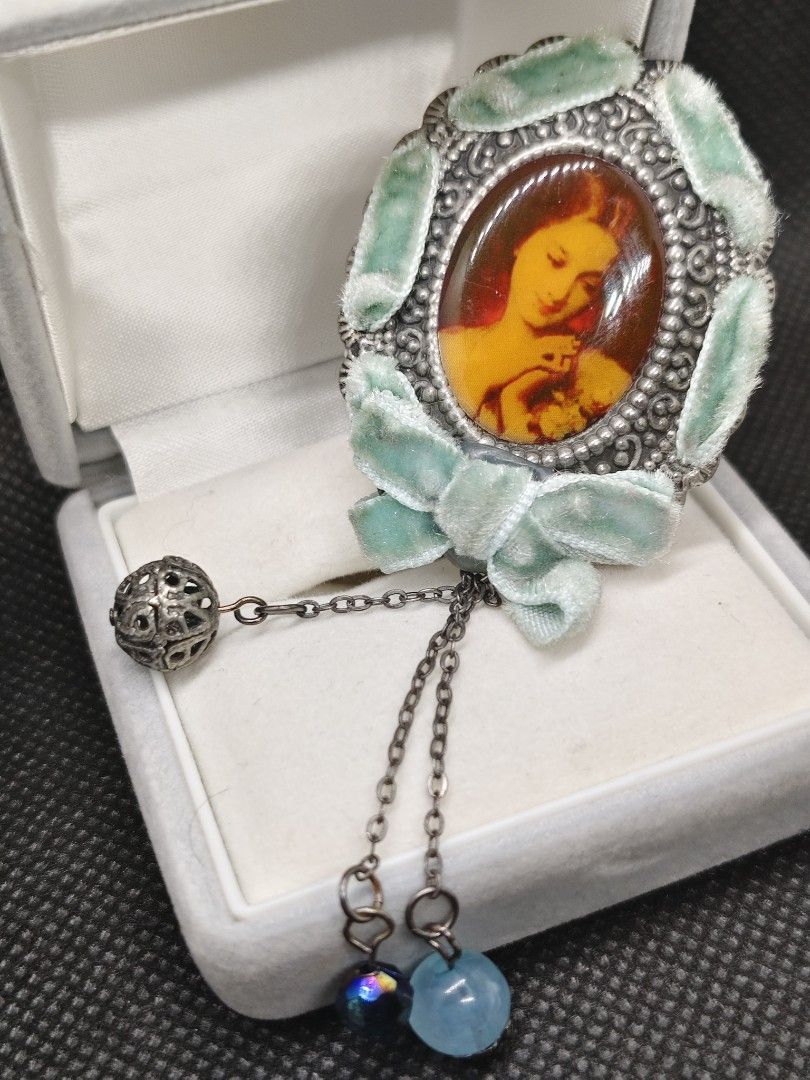 Vintage Oval Brooch with Dangle Charms (Category: Brooches) located in San Mateo. Submitted by joryee (Listing ID 1422312697, Image 3). Description: - Vintage brooch - Oval-shaped design - Features a portrait of a woman and child - Light green velvet trim - Silver-toned metal frame - Includes dangling charms - Pin closure - Comes with a gray velvet box.