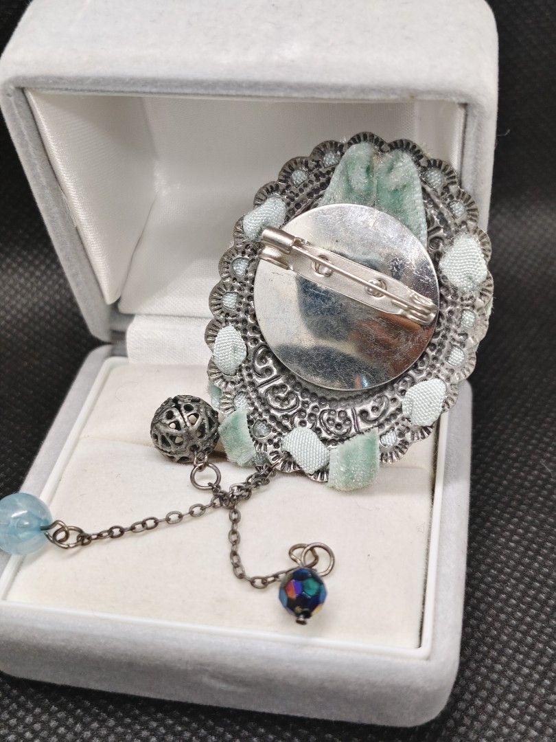 Vintage Oval Brooch with Dangle Charms (Category: Brooches) located in San Mateo. Submitted by joryee (Listing ID 1422312697, Image 2). Description: - Vintage brooch - Oval-shaped design - Features a portrait of a woman and child - Light green velvet trim - Silver-toned metal frame - Includes dangling charms - Pin closure - Comes with a gray velvet box.