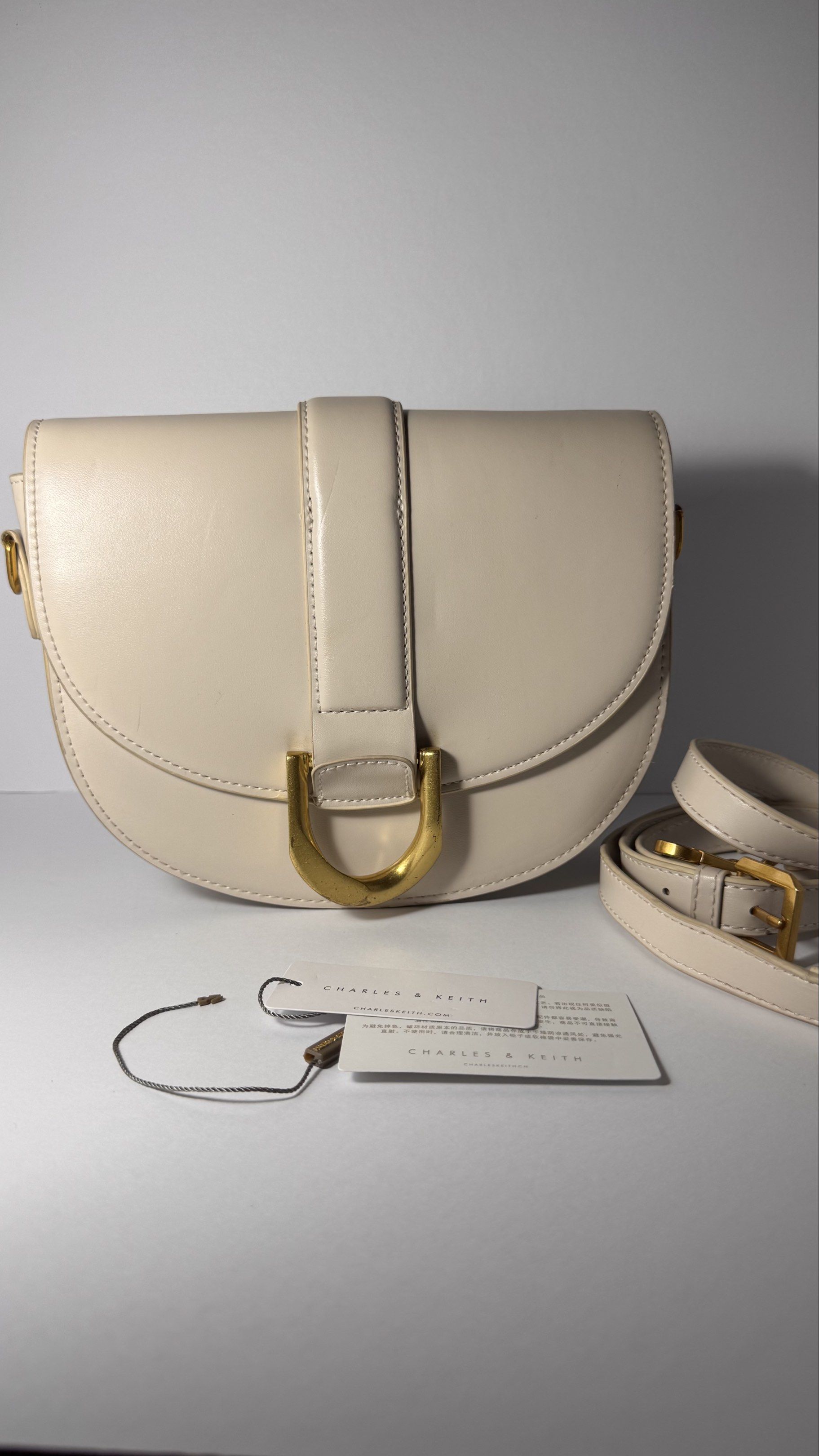 Charles & Keith Saddle Bag (Category: Luxury Bags & Wallets) located in Bacoor. Submitted by neoprelovedjapan (Listing ID 1419261412, Image 1). Description: PreLoved Charles & Keith saddle bag - Features gold-tone buckle and hardware - Includes detachable shoulder strap - Flap closure - Spacious interior - Original tags included - Charles & Keith logo visible.