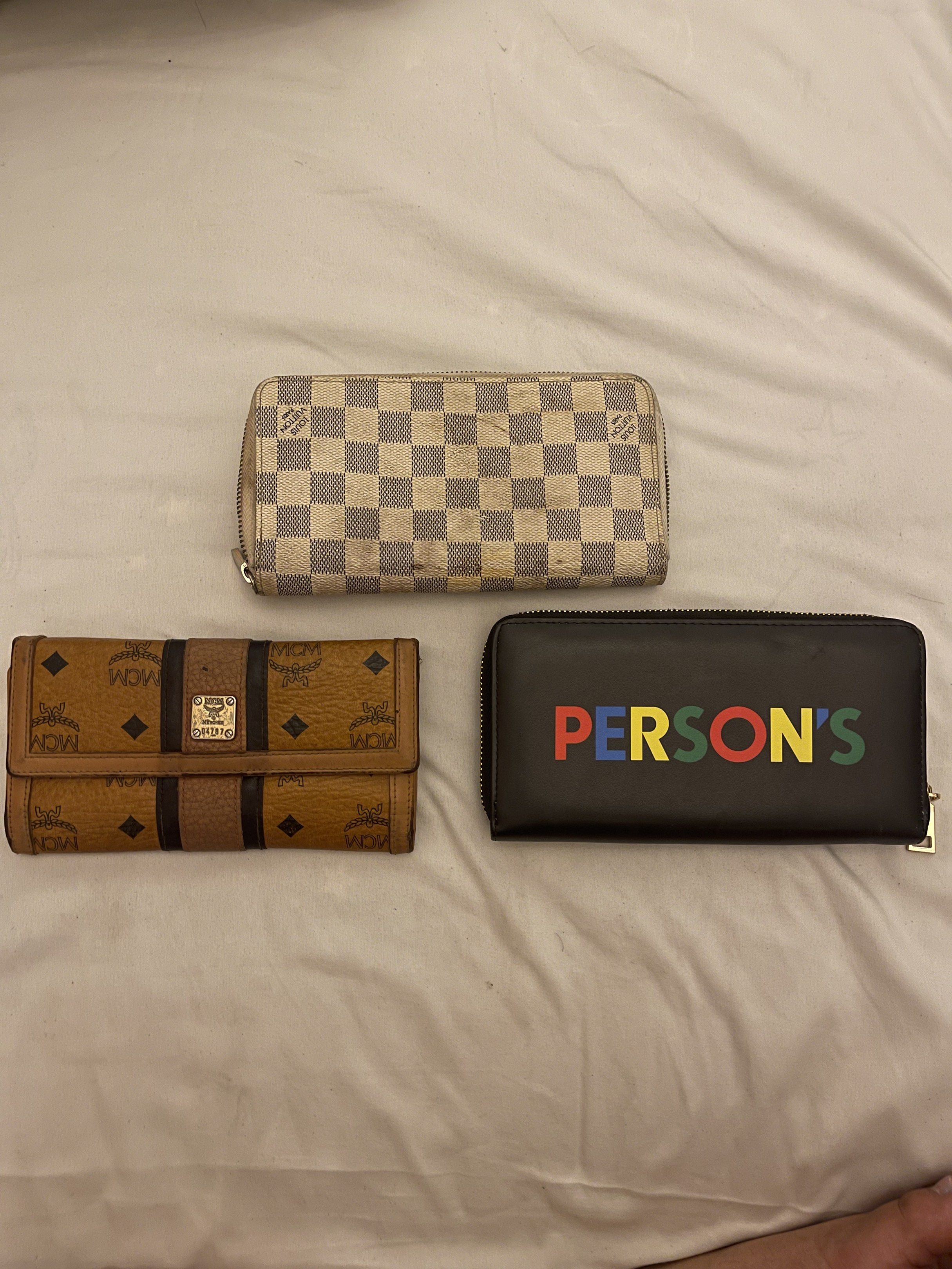 Louis Vuitton, MCM, and Person's Wallets (Category: Luxury Bags & Wallets) located in Marilao. Submitted by wardrovearchives (Listing ID 1419302296, Image 2). Description: - Checkered pattern wallet with zipper (used). - Brown wallet with MCM logo (used). - Black wallet with "PERSON'S" in colorful letters (used). 📌 Sold as bundle only 📌 What you see is what you get 📌 Photos shown are the only photos available 📌 No individual or detailed photo