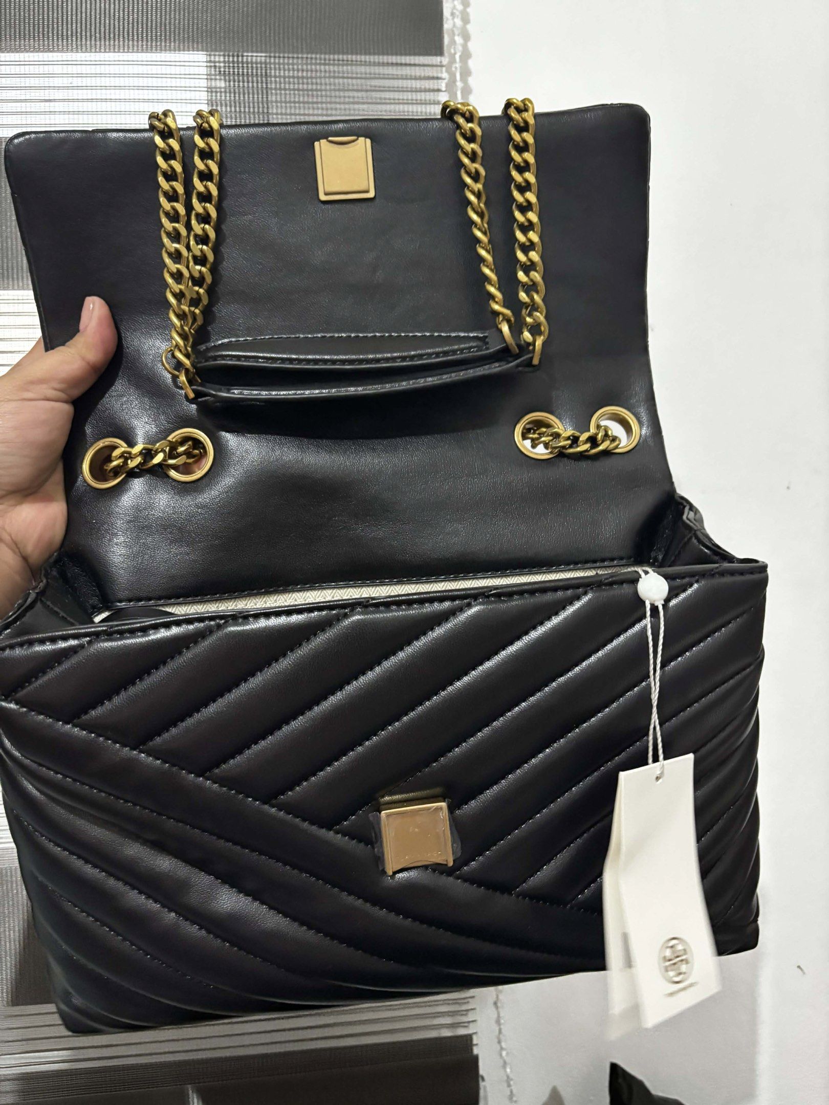 Tory Burch Kira Chevron Shoulder Bag (Category: Luxury Bags & Wallets) located in Magalang. Submitted by katoenjeru0723 (Listing ID 1419295193, Image 2). Description: - Authentic Tory Burch Kira Chevron shoulder bag - Classic black color with gold-tone hardware - Stylish quilted chevron design - Features a convenient chain strap - Secure flap closure with magnetic snap - Includes original tag - Interior with zip pocket - Perfect for everyday use.