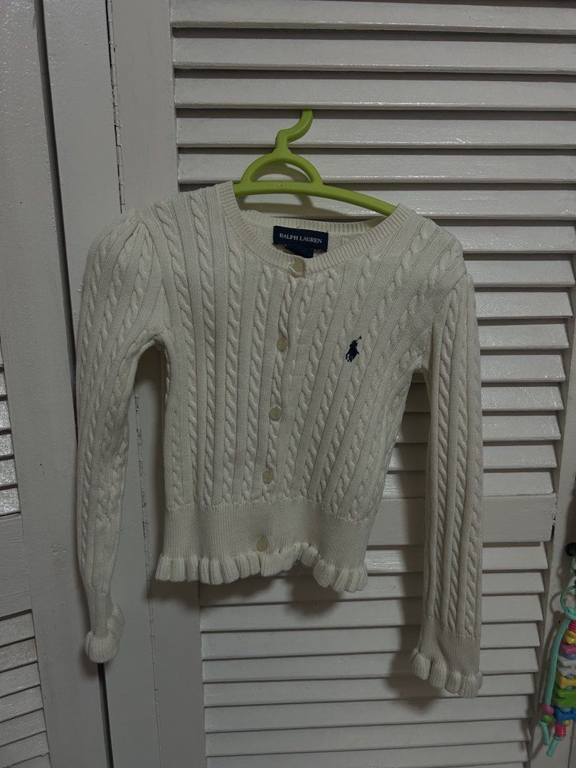 Ralph Lauren Cable Knit Cardigan (Category: Babies & Kids Fashion) located in Manila. Submitted by treenitea (Listing ID 1422463046, Image 1). Description: White cable knit cardigan from Ralph Lauren. It features a button-down front, long sleeves, and a small embroidered logo on the chest. The cardigan has a ruffled hem and cuffs. The size is 4T..