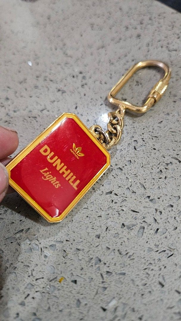 Vintage Dunhill Lights Keychain (Category: Luxury Accessories) located in Alfonso. Submitted by jbcamet (Listing ID 1422426222, Image 2). Description: - Vintage Dunhill Lights keychain - Features a red and gold rectangular pendant - Dunhill Lights logo displayed - Includes a gold-colored chain and key ring - Ideal for collectors and vintage item enthusiasts.