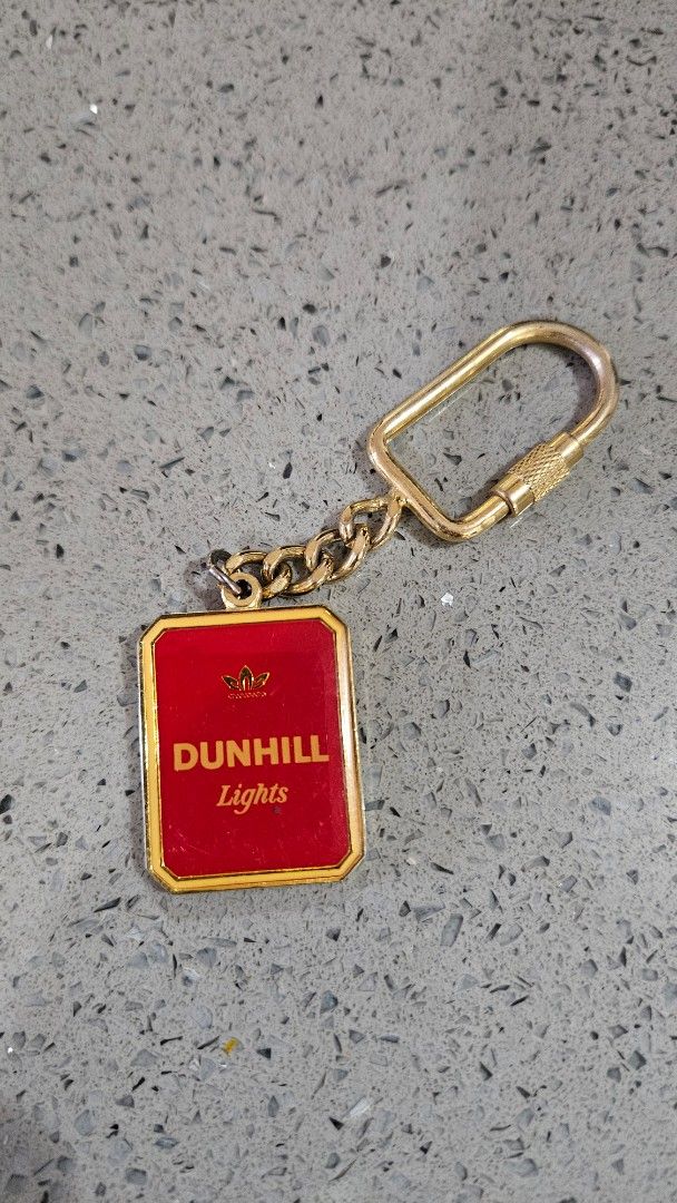 Vintage Dunhill Lights Keychain (Category: Luxury Accessories) located in Alfonso. Submitted by jbcamet (Listing ID 1422426222, Image 1). Description: - Vintage Dunhill Lights keychain - Features a red and gold rectangular pendant - Dunhill Lights logo displayed - Includes a gold-colored chain and key ring - Ideal for collectors and vintage item enthusiasts.