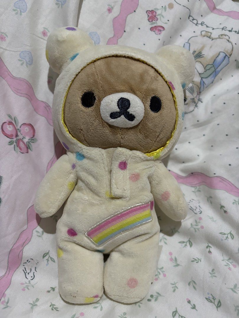 Rilakkuma Bear Plush Toy (Category: Plushies & Soft Toys) located in Manila. Submitted by meloopsy (Listing ID 1422896374, Image 1). Description: - Adorable Rilakkuma bear plush toy. - Features a polka-dot onesie with a rainbow design. - Brown-faced bear with a hood. - Soft and cuddly material. - Perfect for collectors or as a gift. - Includes a tag attached at the back..