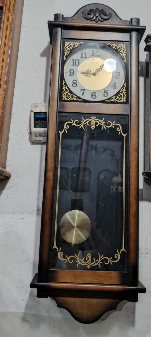 Seiko Quartz Wall Clock (Category: Clocks) located in Caloocan City. Submitted by rowely_jpn (Listing ID 1422748432, Image 3). Description: - Seiko quartz wall clock - Wooden frame - Glass front - Roman numeral clock face - Decorative gold accents - Includes pendulum - Approximately 48 inches tall - In good working condition.