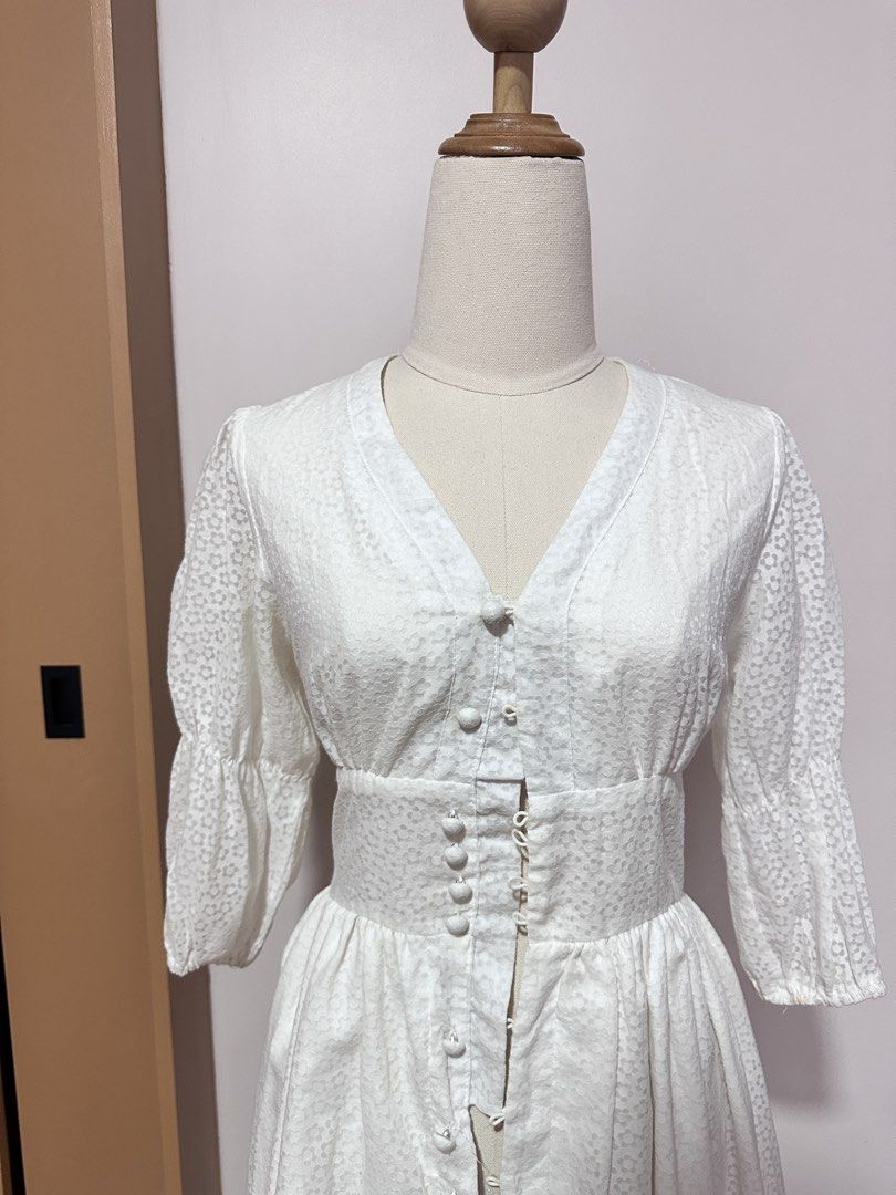 White Floral Dress - Size S (Category: Dresses) located in Tabuk. Submitted by classicseconds (Listing ID 1422766743, Image 3). Description: - White floral dress - Size: S - Features: V-neck, button-down front, fitted waist, flowing skirt, and three-quarter sleeves - Material: Cotton-polyester blend - Care instructions on label.