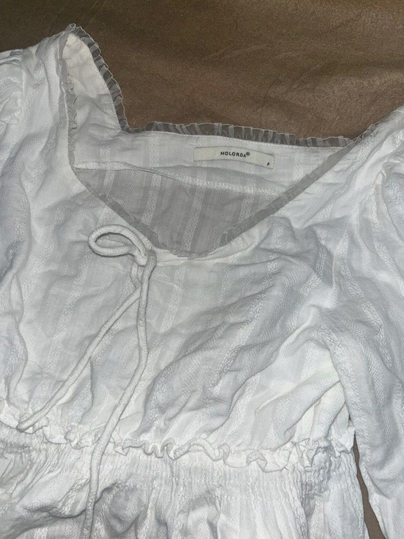 White Long Sleeve Blouse (Category: Blouses) located in Manila. Submitted by quarishop21 (Listing ID 1422827076, Image 3). Description: - MOLORSA white long sleeve blouse - Square neckline with tie detail - Features a ruffled hem - Long sleeves - Textured, striped fabric - Size tag is visible.