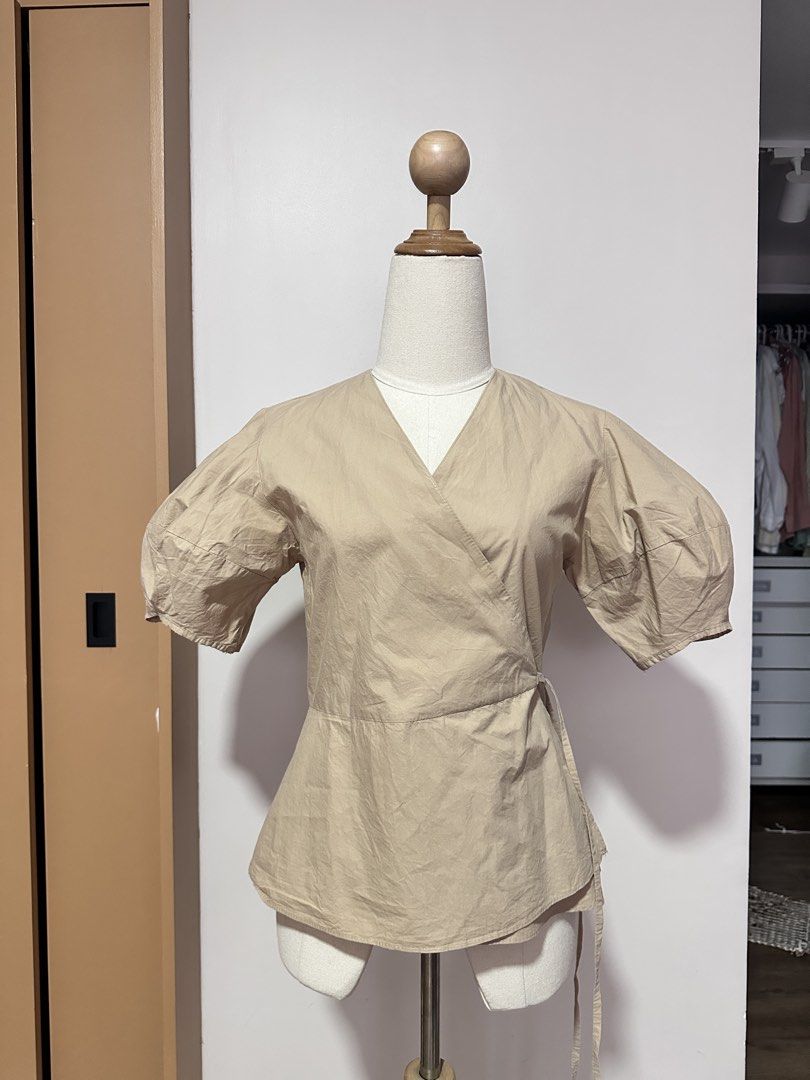 Wrap Top with Puff Sleeves (Category: Blouses) located in Tabuk. Submitted by classicseconds (Listing ID 1422766553, Image 2). Description: - Beige wrap top - V-neckline - Puff sleeves - Tie closure at waist - Adjustable fit - Lightweight fabric - Versatile neutral color - Suitable for casual and semi-formal wear.