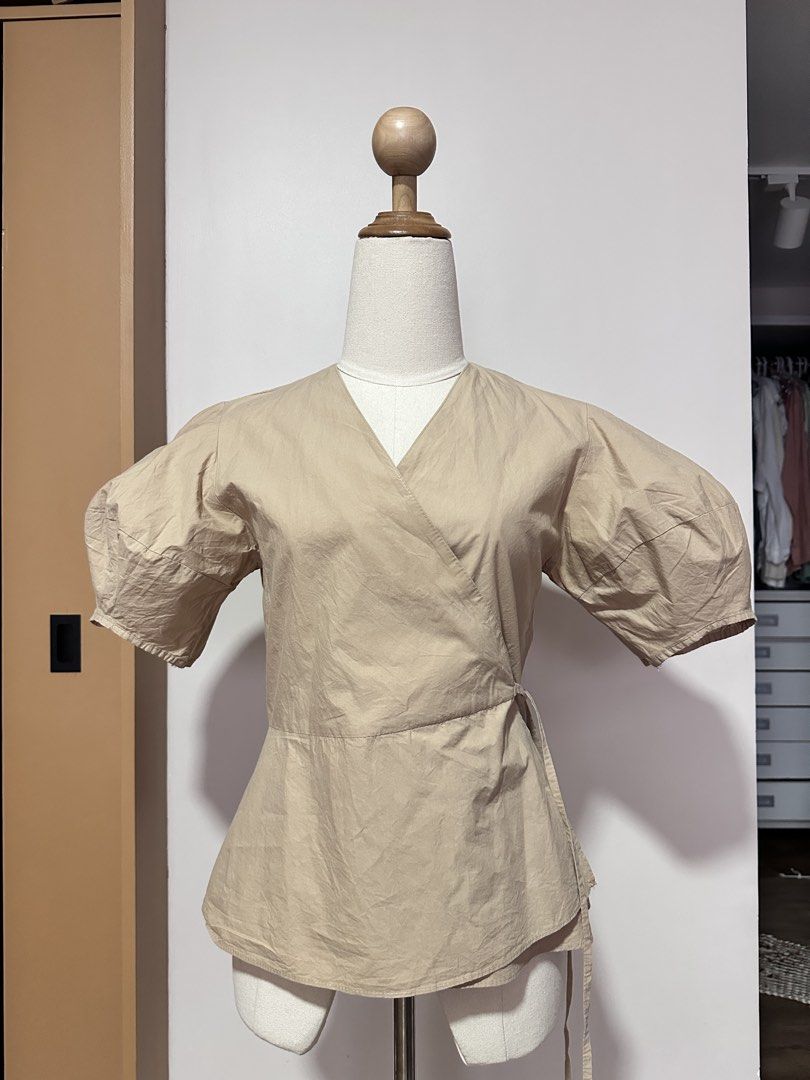 Wrap Top with Puff Sleeves (Category: Blouses) located in Tabuk. Submitted by classicseconds (Listing ID 1422766553, Image 1). Description: - Beige wrap top - V-neckline - Puff sleeves - Tie closure at waist - Adjustable fit - Lightweight fabric - Versatile neutral color - Suitable for casual and semi-formal wear.
