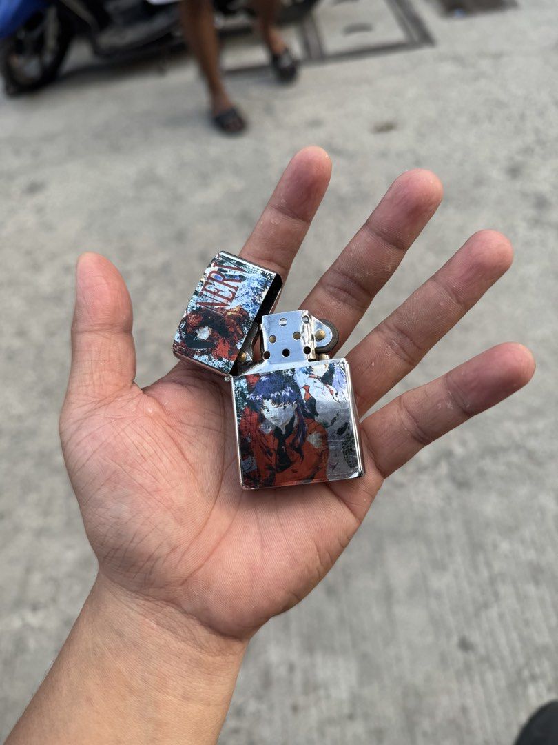 Zippo style Anime collectible lighter (Category: Accessory Holder, Box & Organizers) located in Manila. Submitted by thra_shirts (Listing ID 1422860295, Image 2). Description: This item is a collectible Zippo-style windproof lighter featuring graphic imagery from the anime series Neon Genesis Evangelion, specifically depicting the character Misato Katsuragi and the NERV organization logo. Working Need gas Excellent condition No inclusion .