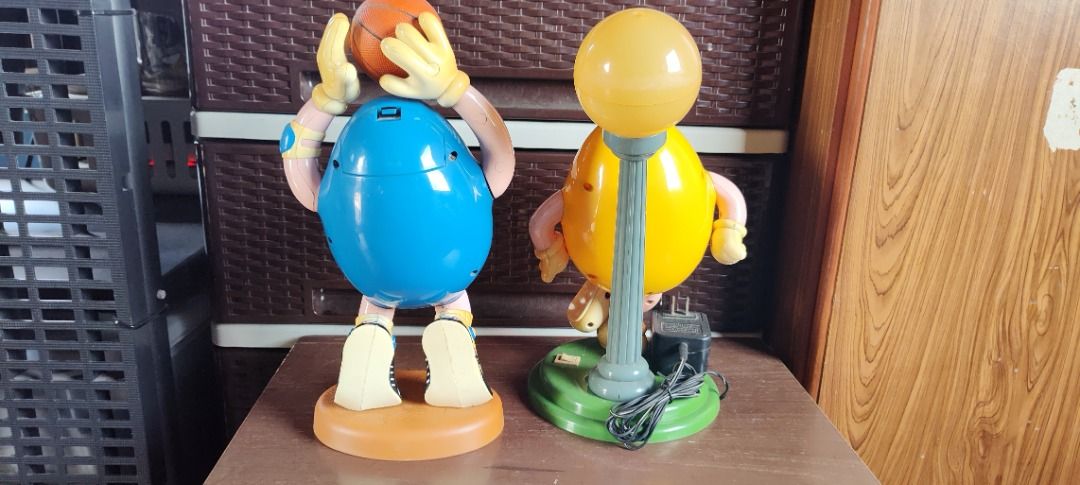 M&M's Figurines Basketball & Lamp (Category: Vintage Collectibles) located in Taguig. Submitted by mckey_1011 (Listing ID 1422958510, Image 3). Description: - Two M&M's figurines included. - Features a blue M&M holding a basketball. - Features a yellow M&M with a lamp. - Basketball M&M has a brown base. - Lamp M&M has a green base. - Both figurines display the M&M's 'M' logo. Note: Table lamp is not working.