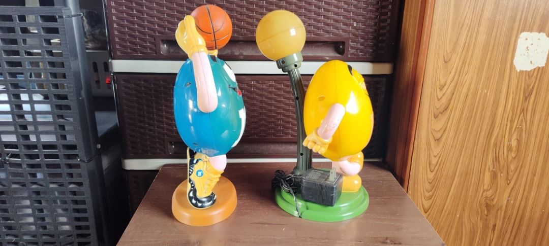 M&M's Figurines Basketball & Lamp (Category: Vintage Collectibles) located in Taguig. Submitted by mckey_1011 (Listing ID 1422958510, Image 2). Description: - Two M&M's figurines included. - Features a blue M&M holding a basketball. - Features a yellow M&M with a lamp. - Basketball M&M has a brown base. - Lamp M&M has a green base. - Both figurines display the M&M's 'M' logo. Note: Table lamp is not working.
