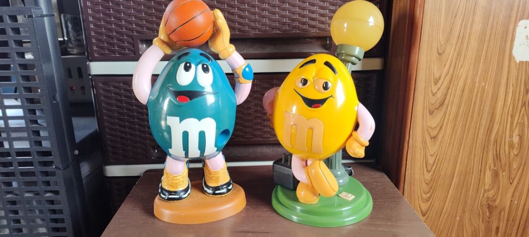 M&M's Figurines Basketball & Lamp (Category: Vintage Collectibles) located in Taguig. Submitted by mckey_1011 (Listing ID 1422958510, Image 1). Description: - Two M&M's figurines included. - Features a blue M&M holding a basketball. - Features a yellow M&M with a lamp. - Basketball M&M has a brown base. - Lamp M&M has a green base. - Both figurines display the M&M's 'M' logo. Note: Table lamp is not working.