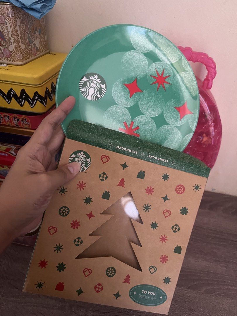 Starbucks Christmas Plate with Box (Category: Dinnerware & Cutlery) located in Cebu City. Submitted by abct1 (Listing ID 1422960188, Image 2). Description: - Starbucks Christmas plate - Festive green design with red star accents - Includes matching Christmas-themed box - Box features a Christmas tree cutout - Plate has the Starbucks logo - Ideal for the holiday season.