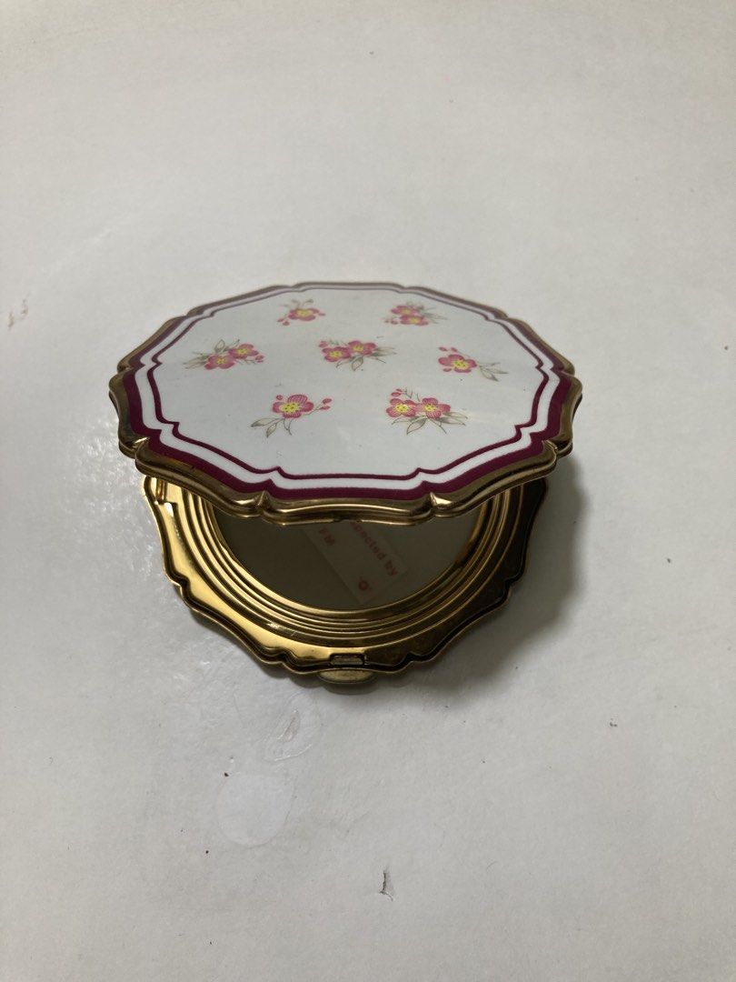 Stratton England Floral Powder Compact (Category: Makeup) located in Plaridel. Submitted by emilia.lily (Listing ID 1423045882, Image 1). Description: - Vintage Stratton England powder compact - White lid with floral design - Gold-tone metal frame - Includes mirror, powder screen, and powder puff - Textured back - Octagonal shape with scalloped edge - Marked 'Stratton England'.