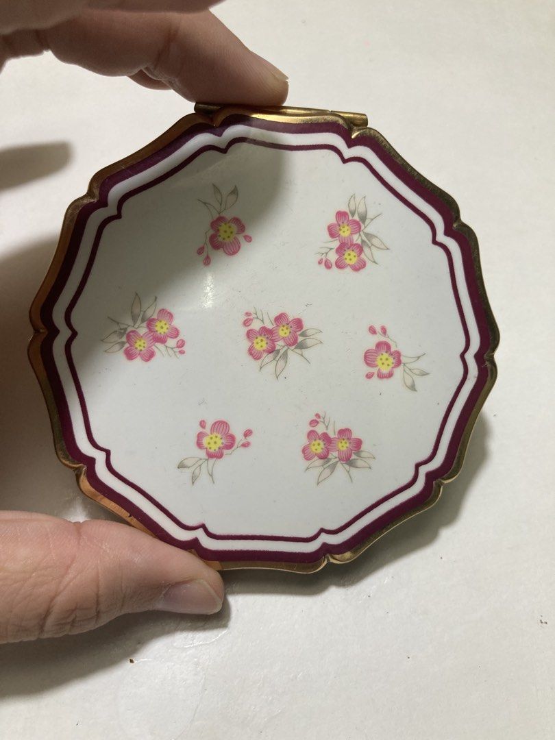 Stratton England Floral Powder Compact (Category: Makeup) located in Plaridel. Submitted by emilia.lily (Listing ID 1423045882, Image 2). Description: - Vintage Stratton England powder compact - White lid with floral design - Gold-tone metal frame - Includes mirror, powder screen, and powder puff - Textured back - Octagonal shape with scalloped edge - Marked 'Stratton England'.