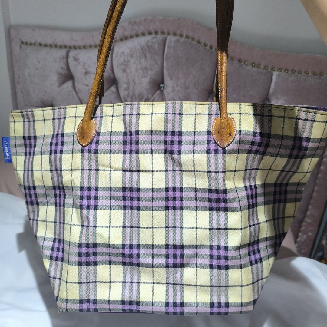 Burberrys Blue Label Tote Bag (Category: Luxury Bags & Wallets) located in Manila. Submitted by yui021 (Listing ID 1423221487, Image 1). Description: - Burberrys Blue Label tote bag with a classic plaid pattern in cream, purple, and black. - Features brown leather handles and a purple interior with a zippered pocket. - Includes a small tag with the Burberrys Blue Label logo. - Flaws shown in the pictures (stain on the canvas, damaged handle).