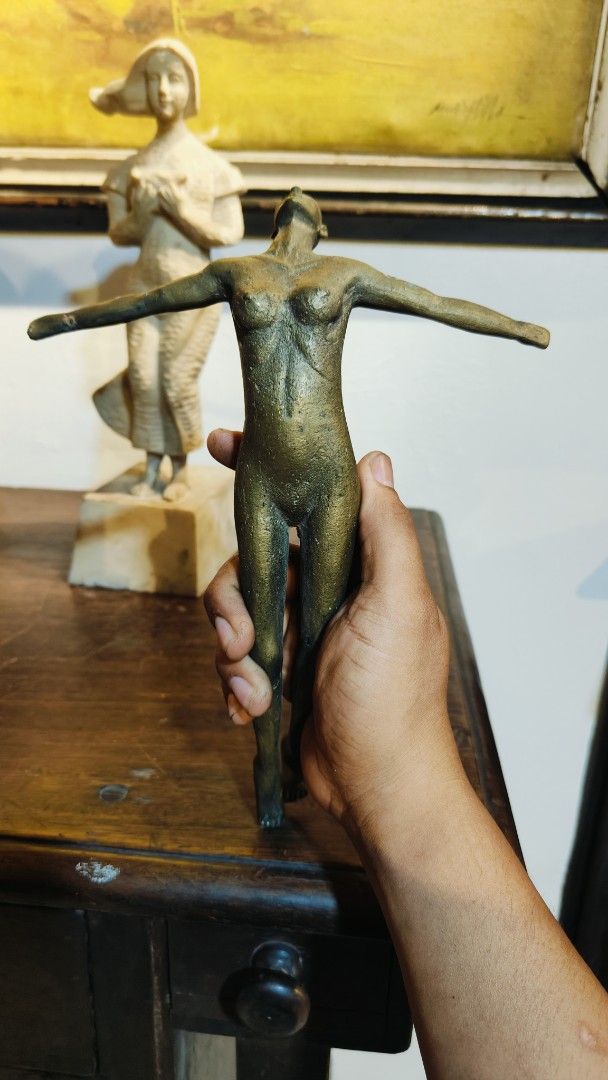 Brass U.P Oblation Sculpture (Category: Other Home Decor) located in Manila. Submitted by makkieenri69972 (Listing ID 1423301386, Image 1). Description: - Bronze sculpture of a female figure - Features outstretched arms - Dark, aged patina - Held in a hand, showcasing details - Stands on a wooden surface - Another sculpture visible in the background.