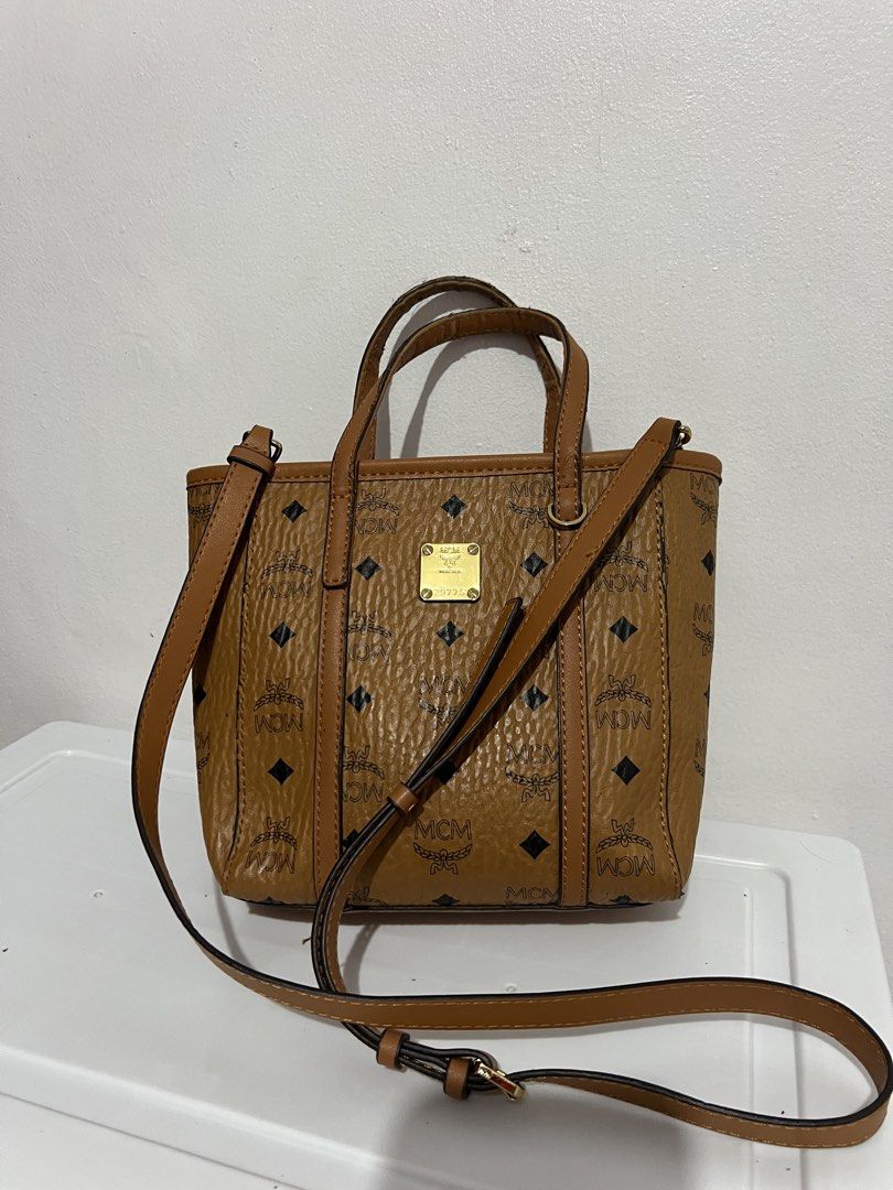 MCM Mini Tote Bag (Category: Luxury Bags & Wallets) located in Manila. Submitted by zoeykim16 (Listing ID 1423327990, Image 1). Description: - Authentic MCM mini tote bag - Brown exterior with MCM logo pattern - Detachable shoulder strap and top handles - Patterned interior lining - Zipper closure - Gold-tone metal logo plate - Minor wear on zipper.