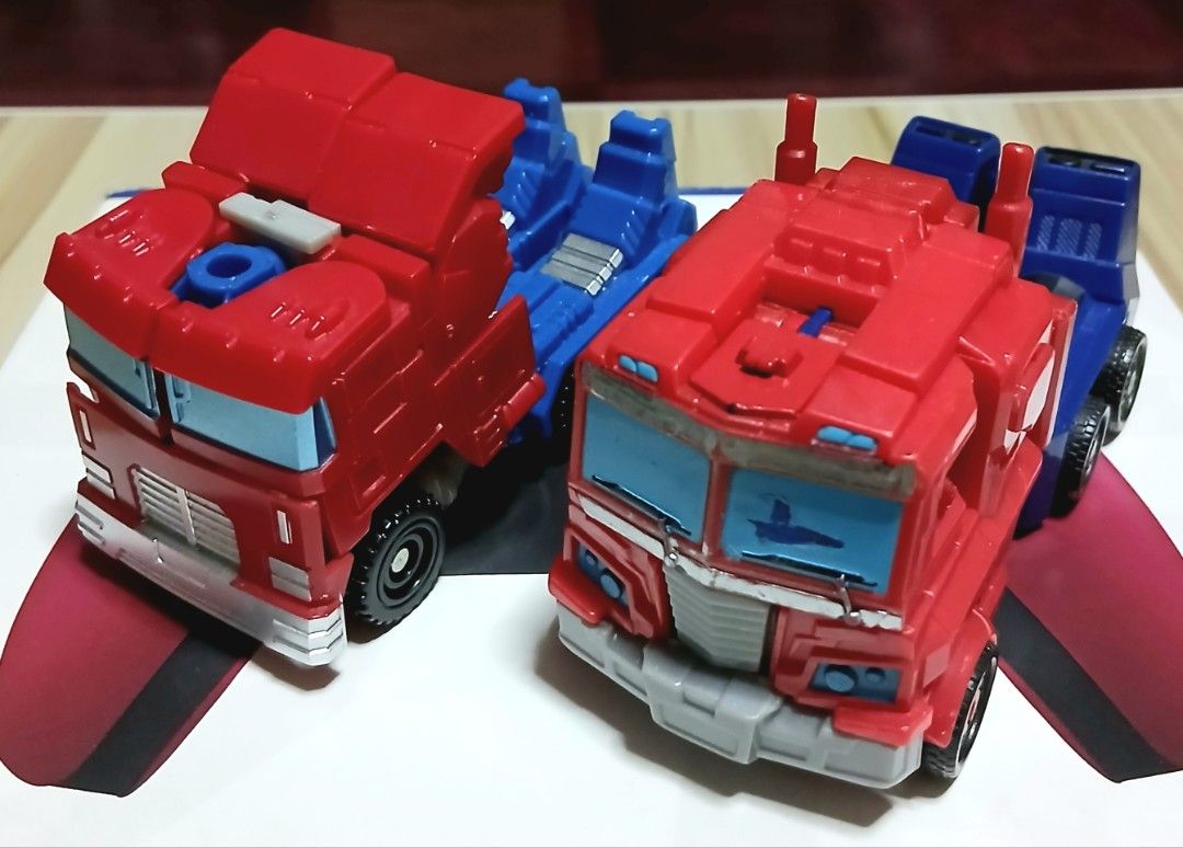 Transformers Optimus Prime Action Figures (Category: Action & Battle Toys) located in Quezon City. Submitted by mrs.maria (Listing ID 1423386485, Image 2). Description: Two Optimus Prime action figures are available. They transform from robot to truck. The figures are red, blue, and silver. One figure is standing, and the other is in truck mode..