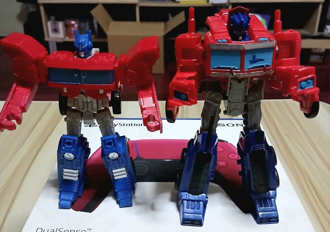 Transformers Optimus Prime Action Figures (Category: Action & Battle Toys) located in Quezon City. Submitted by mrs.maria (Listing ID 1423386485, Image 1). Description: Two Optimus Prime action figures are available. They transform from robot to truck. The figures are red, blue, and silver. One figure is standing, and the other is in truck mode..
