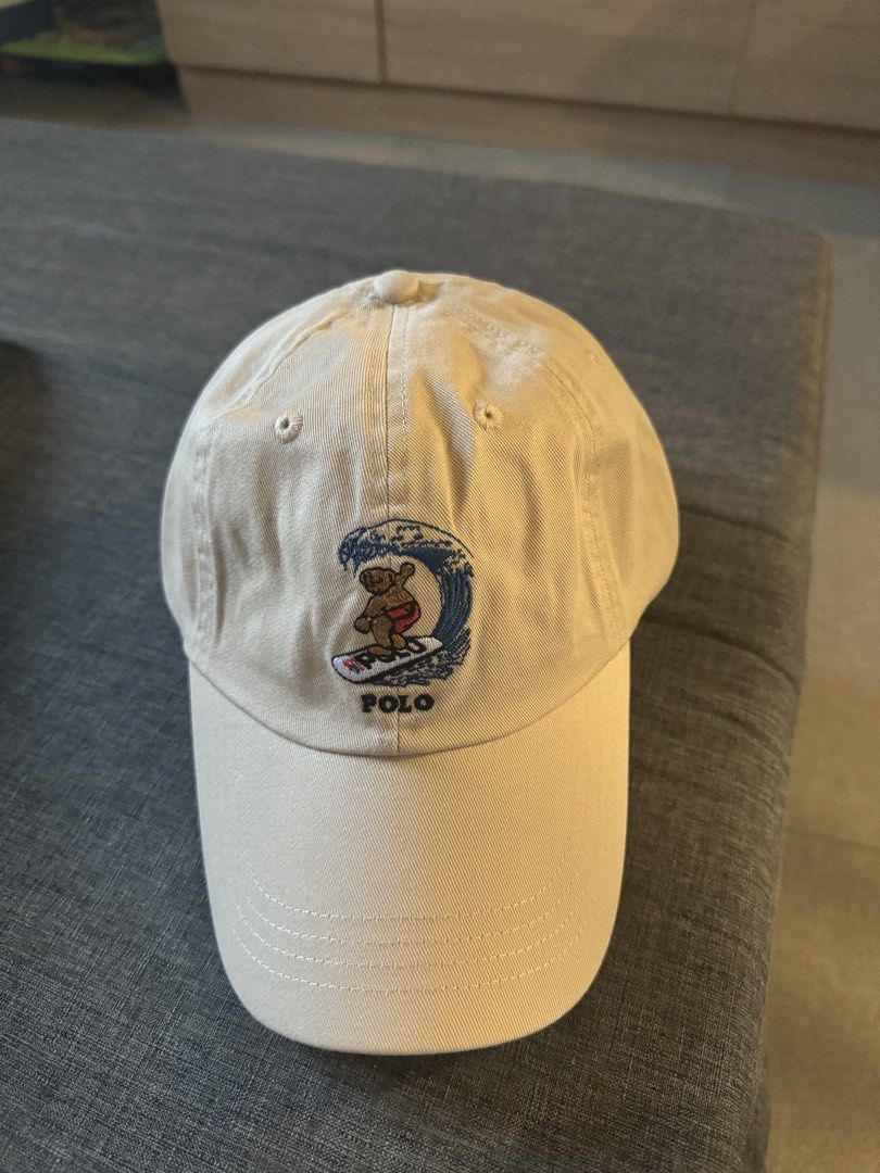 Polo Ralph Lauren Surfing Bear Cap (Category: Caps & Hats) located in San Juan City. Submitted by rlcaps (Listing ID 1423529225, Image 1). Description: Cream-colored cap featuring the Polo Ralph Lauren surfing bear logo embroidered on the front. The cap has a curved brim and a classic six-panel design. The Polo logo is also embroidered below the bear. The cap is made of a soft, durable material..