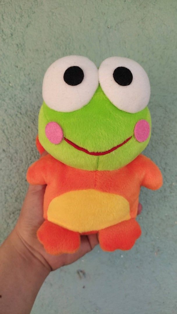 Sanrio Keroppi Plush Toy (Category: Plushies & Soft Toys) located in Tarlac. Submitted by maxgar16638 (Listing ID 1423539109, Image 2). Description: - Adorable Keroppi plush toy - Dressed in an orange outfit - Features a green face, large eyes, and pink cheeks - Made in China - Includes a Sanrio Co., Ltd. tag from 1988, 1998 - Perfect for collectors and gifts.