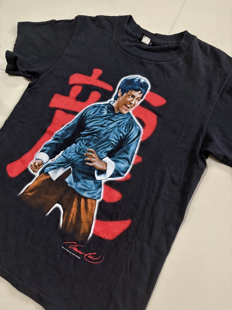 Bruce Lee Vintage T-Shirt (Category: Tshirts & Polo Shirts ) located in Lipa City. Submitted by thriftopia_sj (Listing ID 1423664999, Image 1). Description: - Vintage Bruce Lee t-shirt - Features a front graphic of Bruce Lee in a blue outfit with red Chinese characters - Back of shirt has the Bruce Lee logo in red - From the Bruce Lee Estate - Tag: Changes 20x28 Changes Tag.