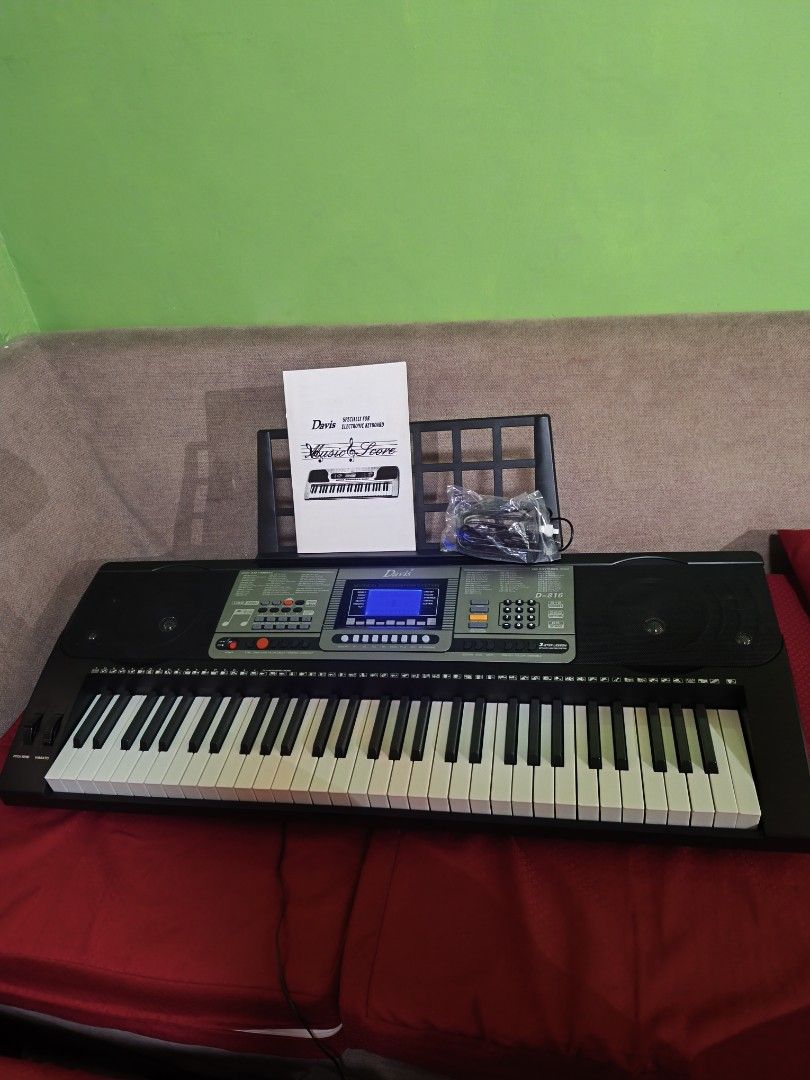 Davis D-816 Digital Keyboard (Category: Musical Instruments) located in Manila. Submitted by bonsai13 (Listing ID 1423694717, Image 3). Description: -Davis 816 Digital Keyboard -61 Touch Sensitive Keys -Light Up Keys -Built in teaching programs -Like new with Box -Bought Feb 20, 2026 -Still under warranty -Includes a music score, power adapter, and a music stand. -The keyboard has a black body with white and black keys..