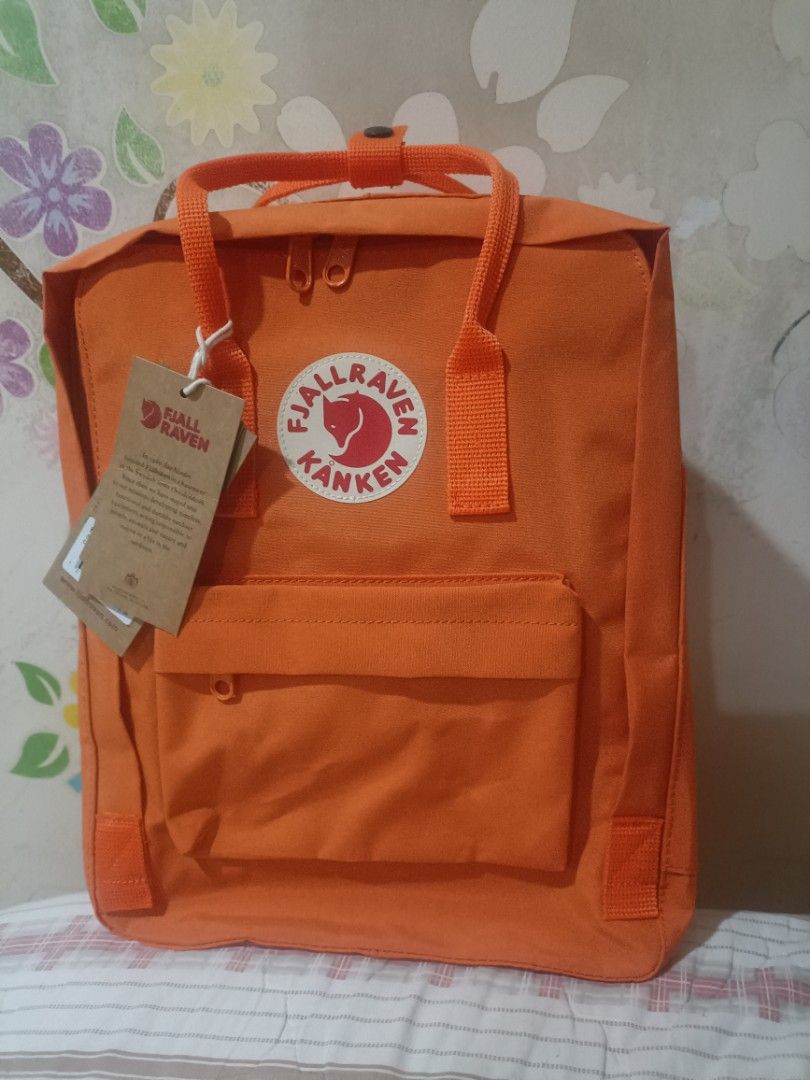 Fjallraven Kanken Classic Backpack - Orange (Category: Backpacks) located in Cebu City. Submitted by dediosmark83726 (Listing ID 1423703676, Image 1). Description: Fjallraven Kanken Classic backpack is in a vibrant orange color. It features the iconic Fjallraven logo on the front and has a classic square design. The backpack includes a front pocket, side pockets, and adjustable straps. The interior has a tag with the Fjallraven logo and informati