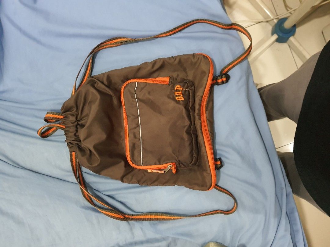 GAP Drawstring Backpack (Category: Backpacks) located in Kuala Lumpur. Submitted by imtheg (Listing ID 1423628183, Image 2). Description: - Good Condition - GAP drawstring backpack - Brown body with orange accents - Front zip pocket with GAP logo - Orange and brown striped straps - Made of nylon-like material - Simple and practical design.