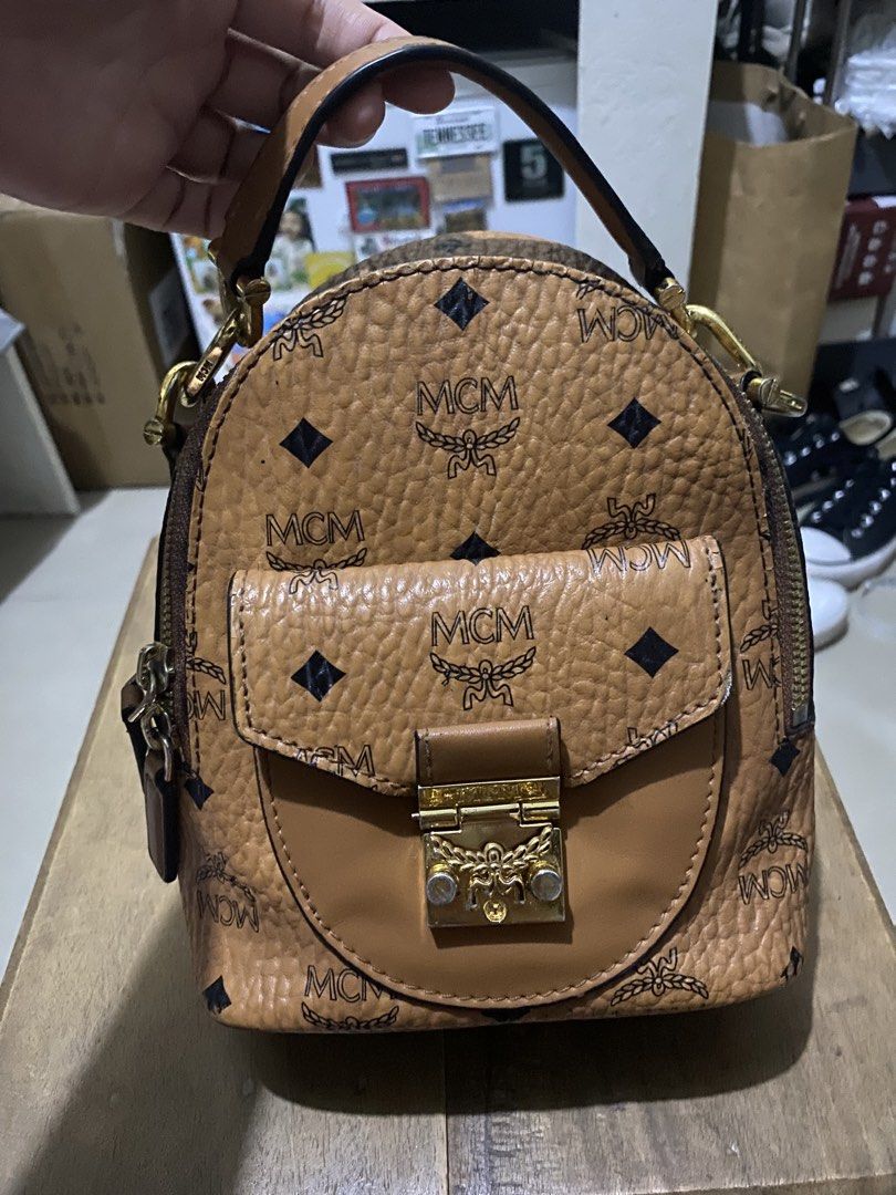 MCM X-Mini Tracy Backpack in Visetos Cognac (Category: Luxury Bags & Wallets) located in Munoz. Submitted by harm0nica337 (Listing ID 1423743950, Image 1). Description: Thrifted item, unknown authenticity but it has white tag with its code inside Visetos Cognac color - Top handle and adjustable straps - Flap closure with gold-tone clasp - Detachable strap included Flaws: wear on straps and hardware, fabric inner oil stain and smell, rubber lining