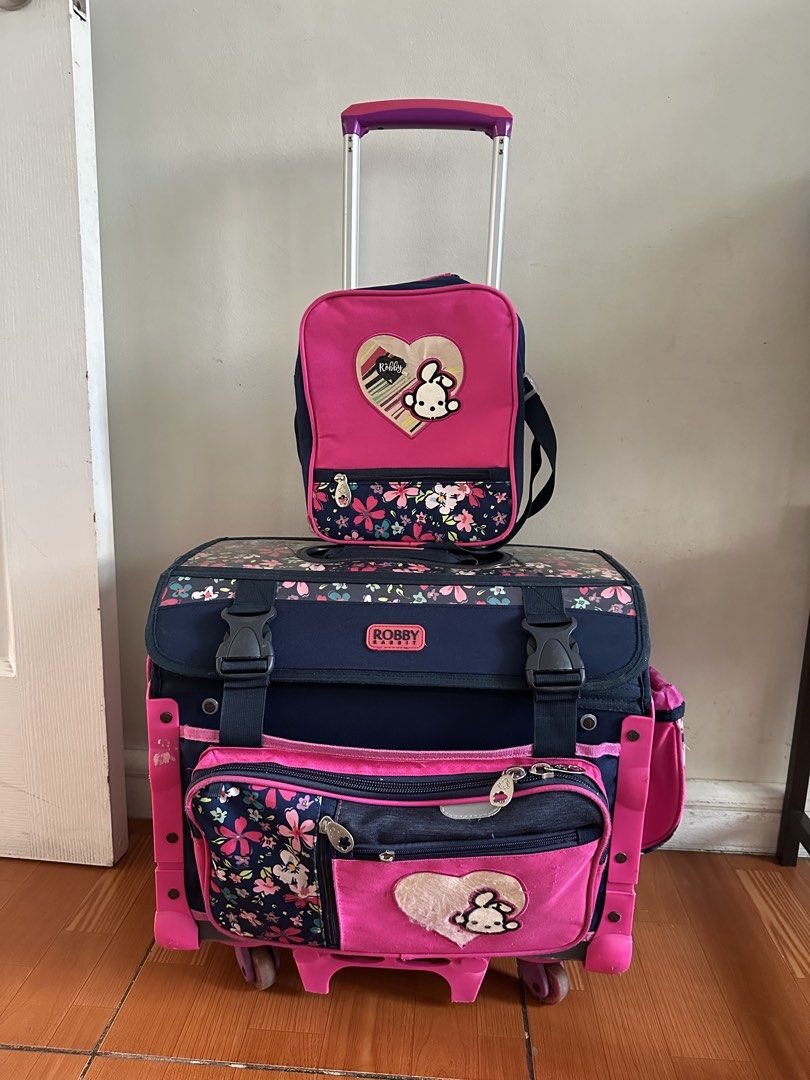 Robby Rabbit trolley school bag (Category: Babies & Kids Fashion) located in Cainta. Submitted by kath_pl (Listing ID 1423639381, Image 1). Description: Robby Rabbit rolling backpack set includes a rolling backpack, a detachable small bag, and a pencil case. The set features a pink and navy blue floral design with a cute bunny motif. The backpack has multiple compartments and a retractable handle..