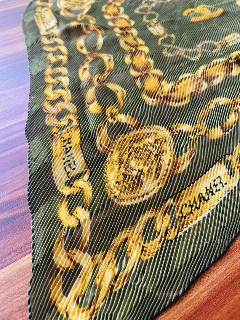 Chanel Pleated Chain Print Scarf (Category: Luxury Accessories) located in Oroquieta. Submitted by mightyfalcon.f3b3e6 (Listing ID 1423912237, Image 3). Description: - Chanel scarf - Features a chain print design - Pleated texture and square shape - Gold and olive green color scheme - Chanel logo visible - Made of lightweight material.