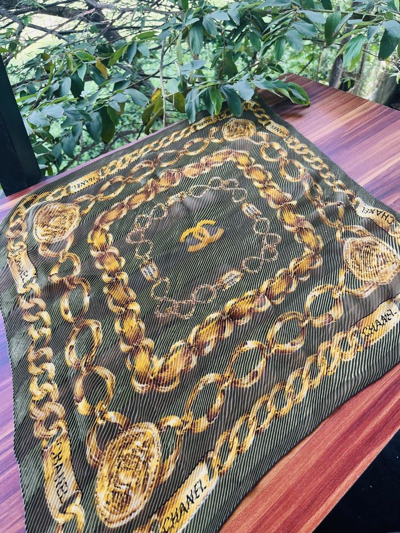 Chanel Pleated Chain Print Scarf (Category: Luxury Accessories) located in Oroquieta. Submitted by mightyfalcon.f3b3e6 (Listing ID 1423912237, Image 1). Description: - Chanel scarf - Features a chain print design - Pleated texture and square shape - Gold and olive green color scheme - Chanel logo visible - Made of lightweight material.