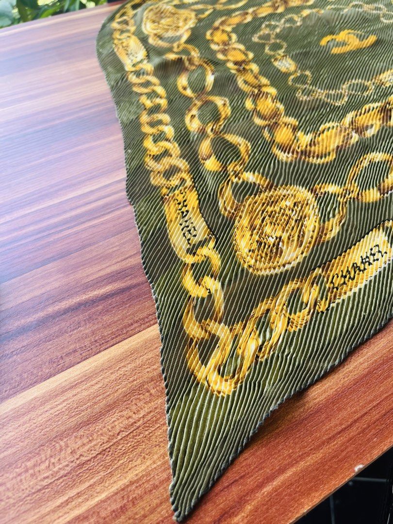 Chanel Pleated Chain Print Scarf (Category: Luxury Accessories) located in Oroquieta. Submitted by mightyfalcon.f3b3e6 (Listing ID 1423912237, Image 2). Description: - Chanel scarf - Features a chain print design - Pleated texture and square shape - Gold and olive green color scheme - Chanel logo visible - Made of lightweight material.