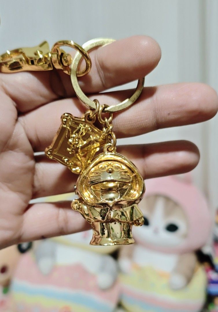 Doraemon Metal Keychain (Heavy) (Category: Character Goods) located in Manila. Submitted by yourfavoritethings7 (Listing ID 1423970301, Image 1). Description: - Gold-colored keychain - Features a Doraemon charm - Includes a small square charm with text on the back - Comes with a clasp for easy attachment - Ideal accessory for Doraemon enthusiasts.