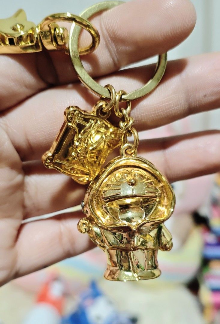 Doraemon Metal Keychain (Heavy) (Category: Character Goods) located in Manila. Submitted by yourfavoritethings7 (Listing ID 1423970301, Image 2). Description: - Gold-colored keychain - Features a Doraemon charm - Includes a small square charm with text on the back - Comes with a clasp for easy attachment - Ideal accessory for Doraemon enthusiasts.