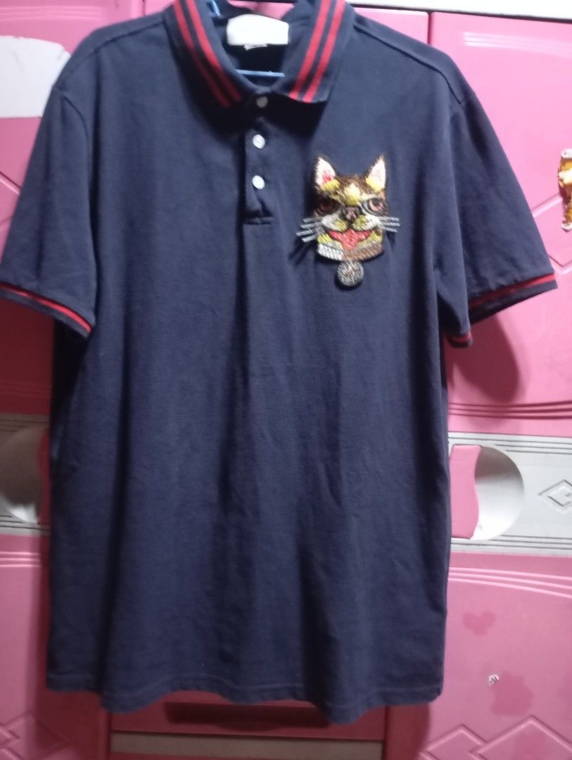 Gucci Cat Embroidered Polo Shirt (Category: Tshirts & Polo Shirts ) located in Adams. Submitted by odddragon-f00047 (Listing ID 1423969669, Image 1). Description: - Gucci navy blue polo shirt - Embroidered cat design on chest - Red and navy striped collar - Button-down placket 20x27 - Short sleeves - Made in Italy.