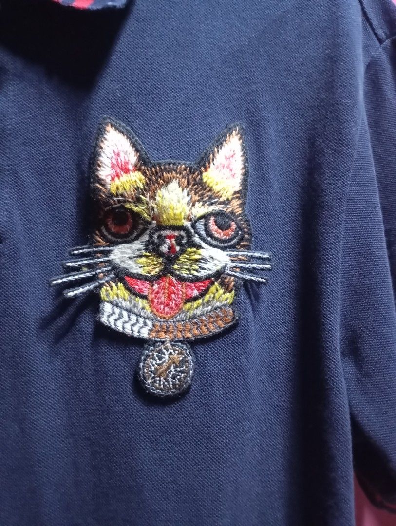 Gucci Cat Embroidered Polo Shirt (Category: Tshirts & Polo Shirts ) located in Adams. Submitted by odddragon-f00047 (Listing ID 1423969669, Image 2). Description: - Gucci navy blue polo shirt - Embroidered cat design on chest - Red and navy striped collar - Button-down placket 20x27 - Short sleeves - Made in Italy.