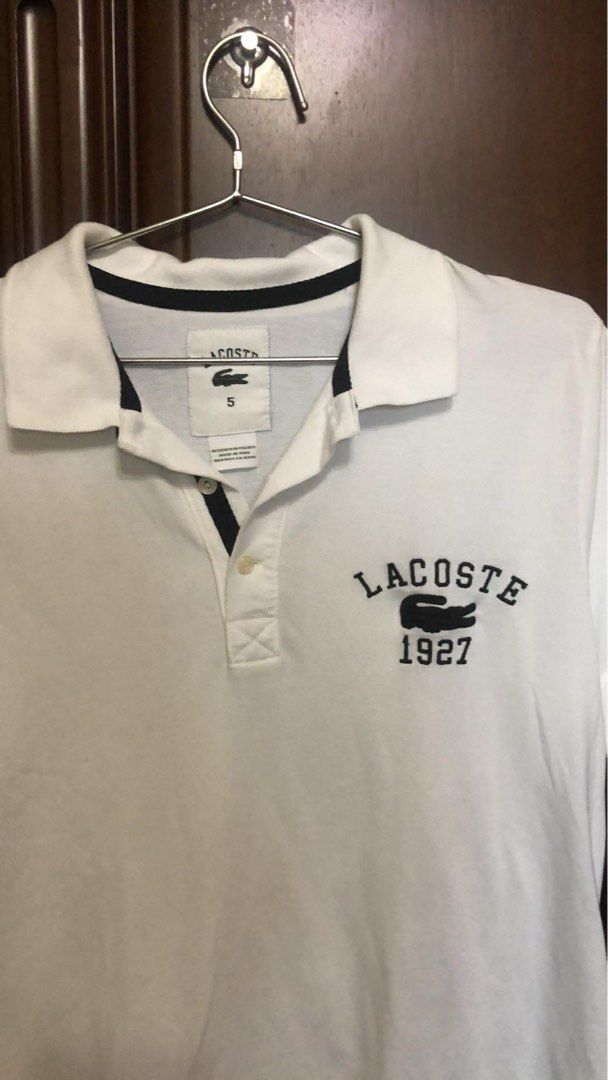 Lacoste 1927 White Polo Shirt (Category: Tshirts & Polo Shirts ) located in Batac City. Submitted by paudeclutterz (Listing ID 1423842381, Image 3). Description: - Lacoste polo shirt - Features the 1927 logo - Size 5 - Classic polo collar and short sleeves - Navy blue trim on collar and sleeves - Made of 100% cotton - Made in Peru - Designed in France.