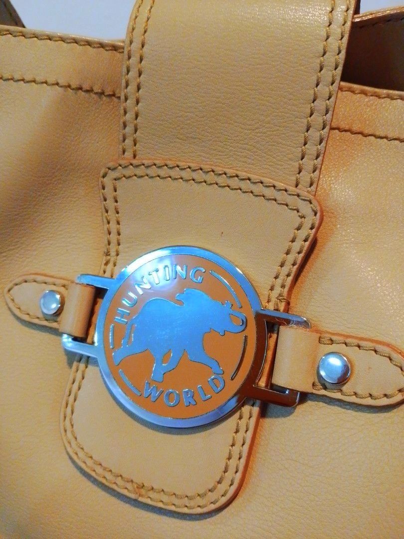 Shoulder bag Hunting world genuine leather (Category: Luxury Bags & Wallets) located in Cabanatuan. Submitted by miss.maia (Listing ID 1417802349, Image 2). Description: Brand: Hunting World Material: Primarily leather, though some Hunting World bags also incorporate their signature "Battue Cloth" nylon material with leather trim. Color: Beige/Tan Features: Elephant logo hardware on the front clasp. Buckled shoulder strap details. Open exterior p