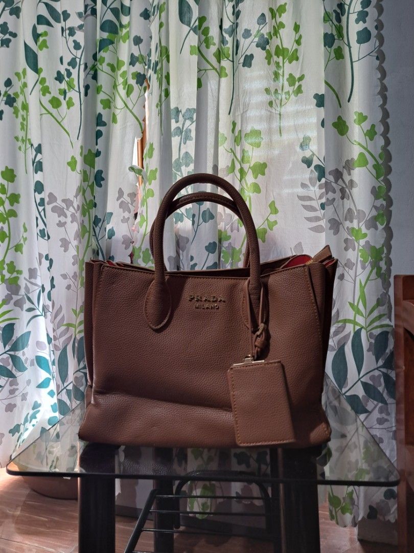 Prada Milano Brown Bag (Category: Luxury Bags & Wallets) located in Mandaluyong City. Submitted by teeniethriftee (Listing ID 1419450657, Image 1). Description: - Brown Prada Milano tote bag - Top handle design - Includes a small attached pouch - Red interior lining - Features a zippered compartment - Gold Prada Milano logo - Made of leather - bought from canada. - with sign of usages but can be repaired by the buyer..