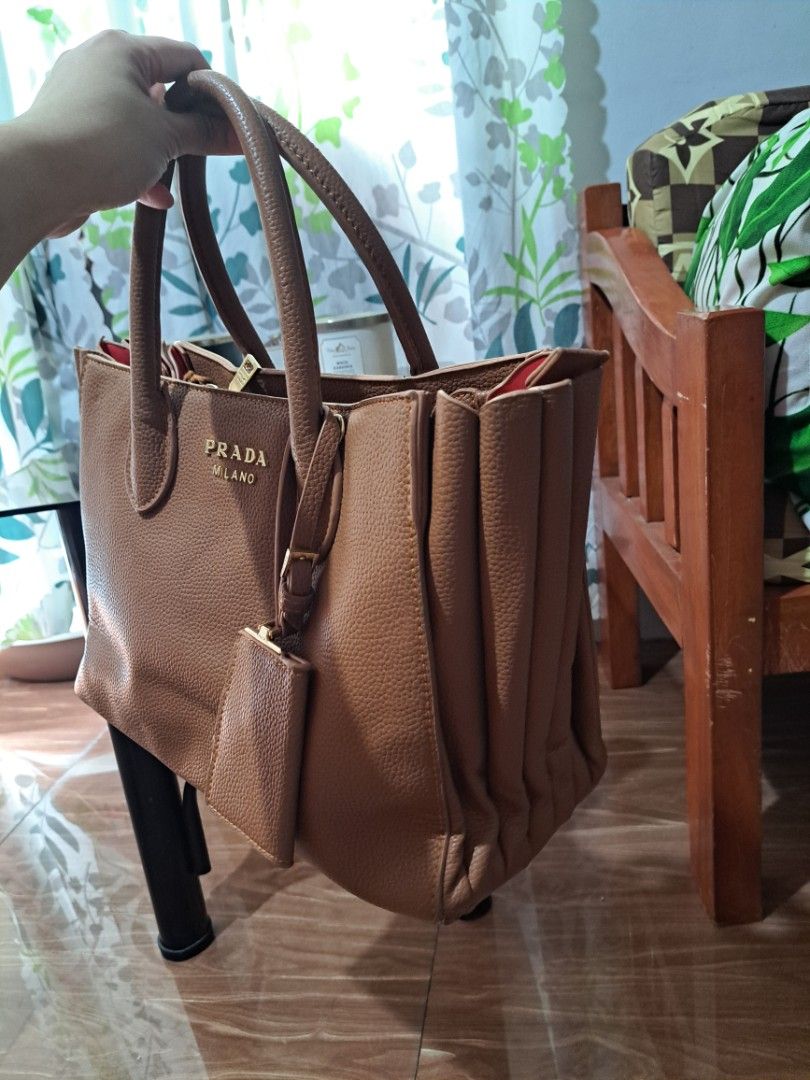 Prada Milano Brown Bag (Category: Luxury Bags & Wallets) located in Mandaluyong City. Submitted by teeniethriftee (Listing ID 1419450657, Image 3). Description: - Brown Prada Milano tote bag - Top handle design - Includes a small attached pouch - Red interior lining - Features a zippered compartment - Gold Prada Milano logo - Made of leather - bought from canada. - with sign of usages but can be repaired by the buyer..
